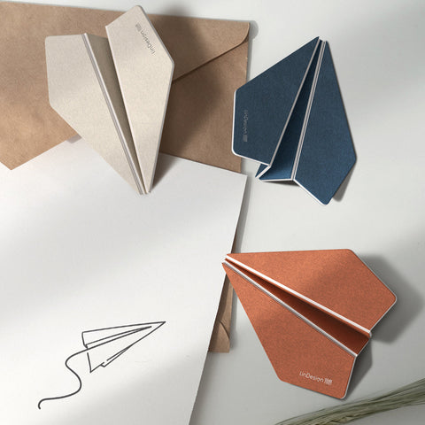 Colorful paper airplane-shaped cards on a light surface with a white card and pen.