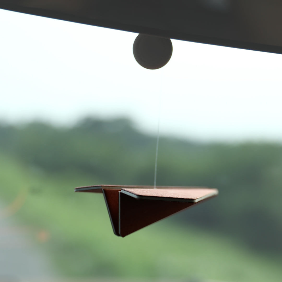 Car air freshener hanging from a car's rearview mirror with a blurred outdoor background