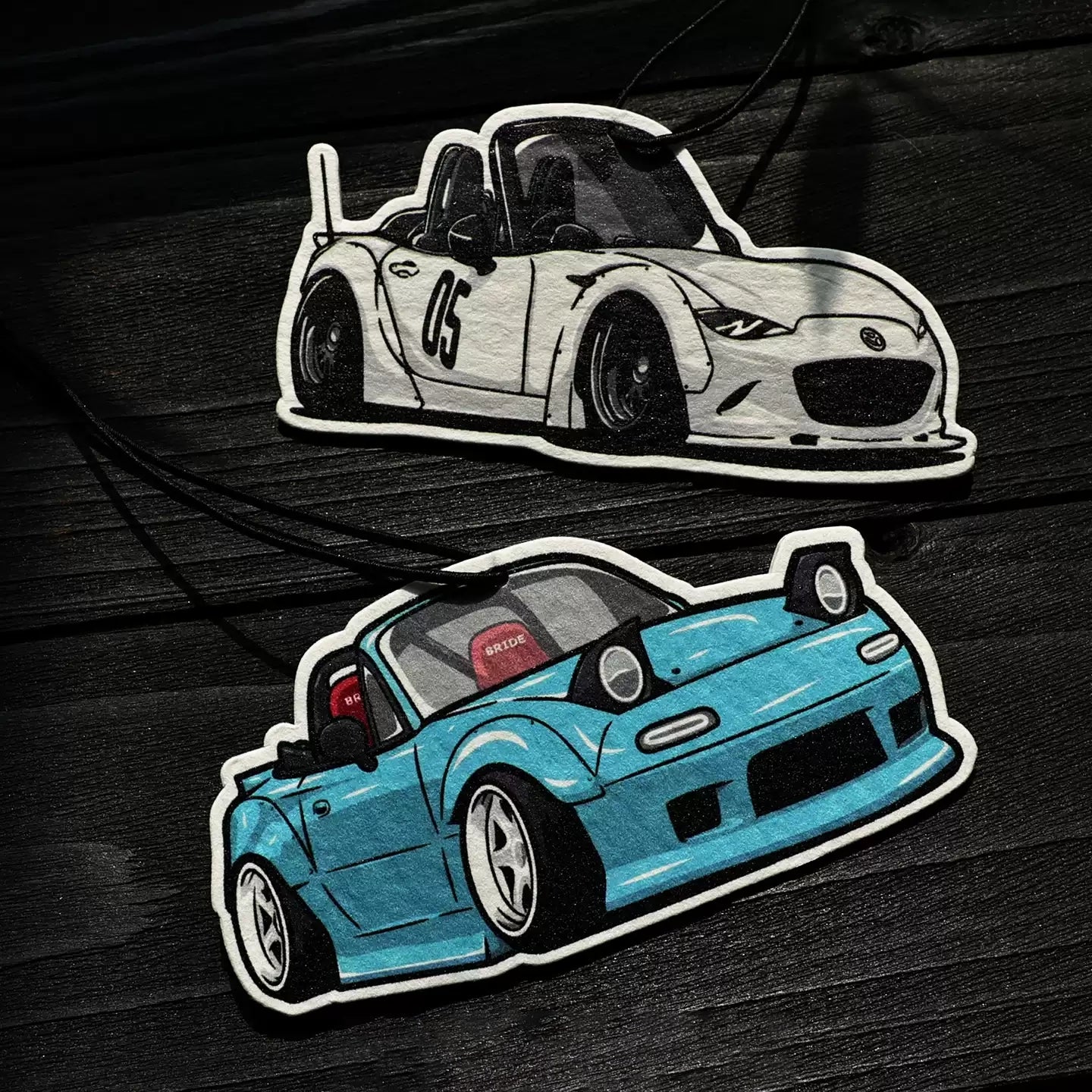 Two car stickers on a dark wooden surface, one white and one blue.