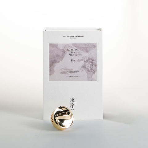 Gold decorative item in front of a white box with gray design on a light gray background