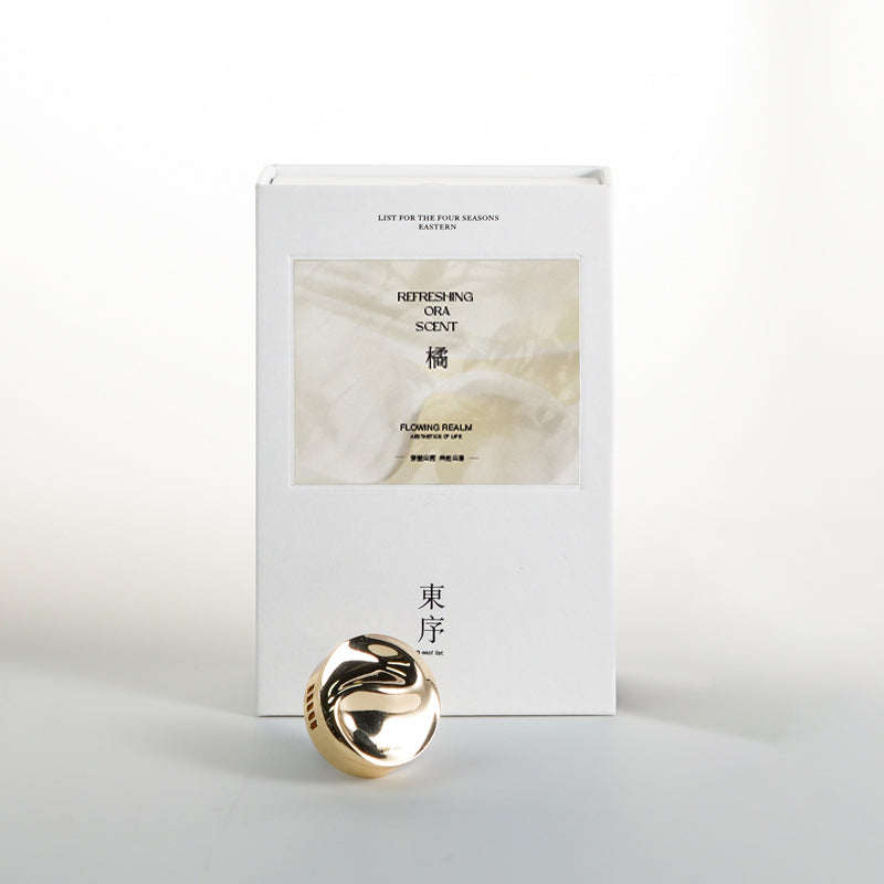Gold decorative item with a white box labeled 'Ora Scent' on a light gray background