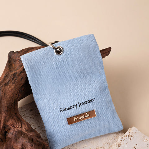 Light blue sensory pouch with 'Sensory Journey' and 'Fumyrah' text, placed on a natural wood and stone background.