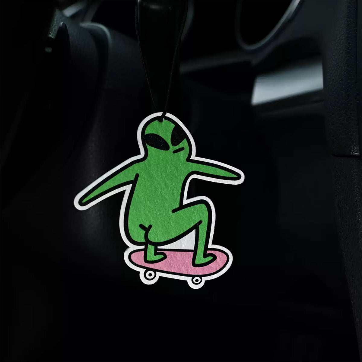 Green alien on a pink skateboard air freshener hanging from a car's rearview mirror.