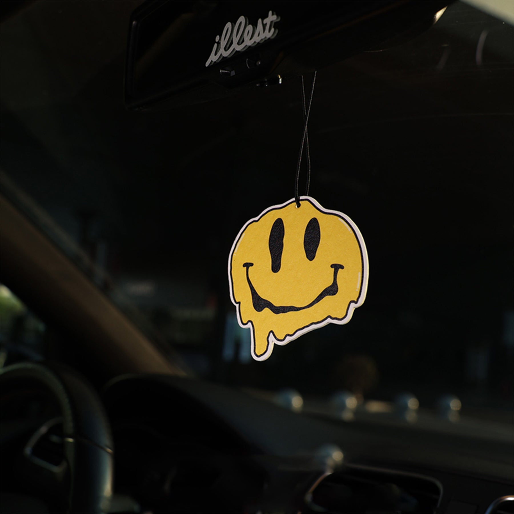 Yellow smiley face air freshener hanging from a car's rearview mirror.