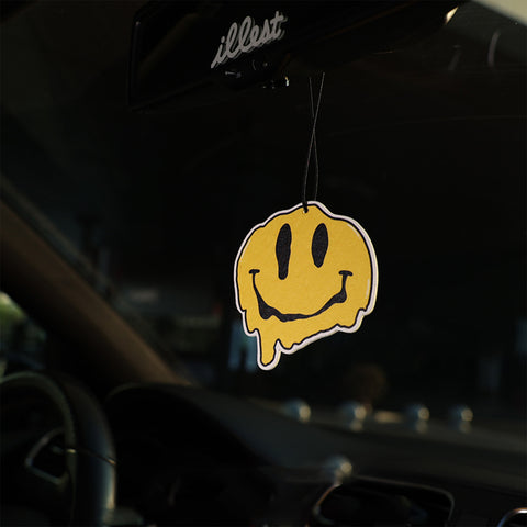 Yellow smiley face air freshener hanging from a car's rearview mirror.