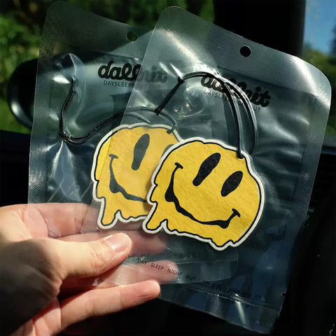 Two yellow smiley face air fresheners in clear packaging held by a hand.