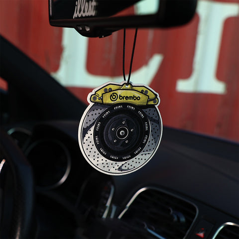 Car air freshener shaped like a brake rotor with Brembo logo hanging from a car's rearview mirror.