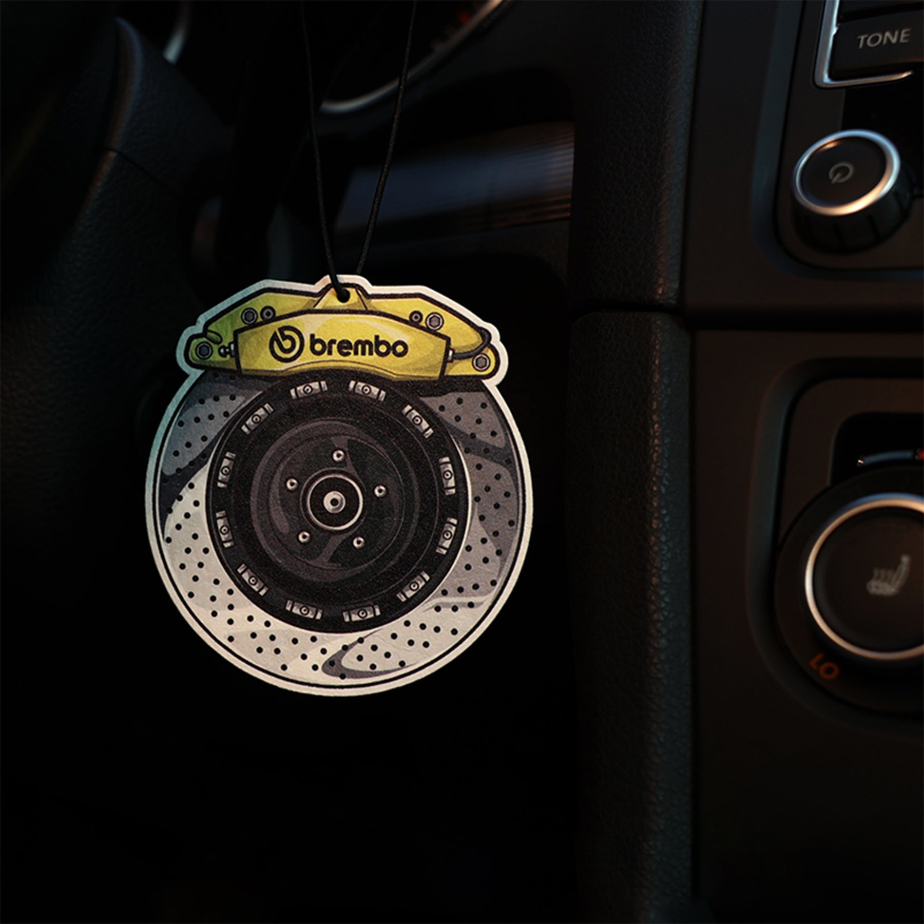 Car air freshener shaped like a brake disc with Brembo logo hanging in a car's interior.
