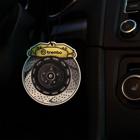 Car air freshener shaped like a brake disc with Brembo logo hanging in a car's interior.