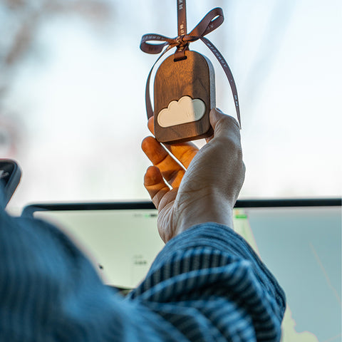 Person holding a wooden ornament with a cloud design against a blurred indoor background