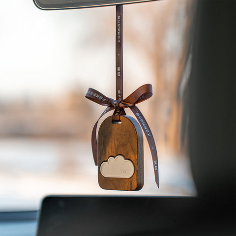 Wooden car hanging ornament with cloud design on a blurred car interior background