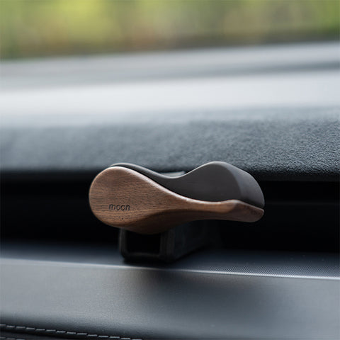 Wooden car phone holder on a car dashboard with 'moon' branding.