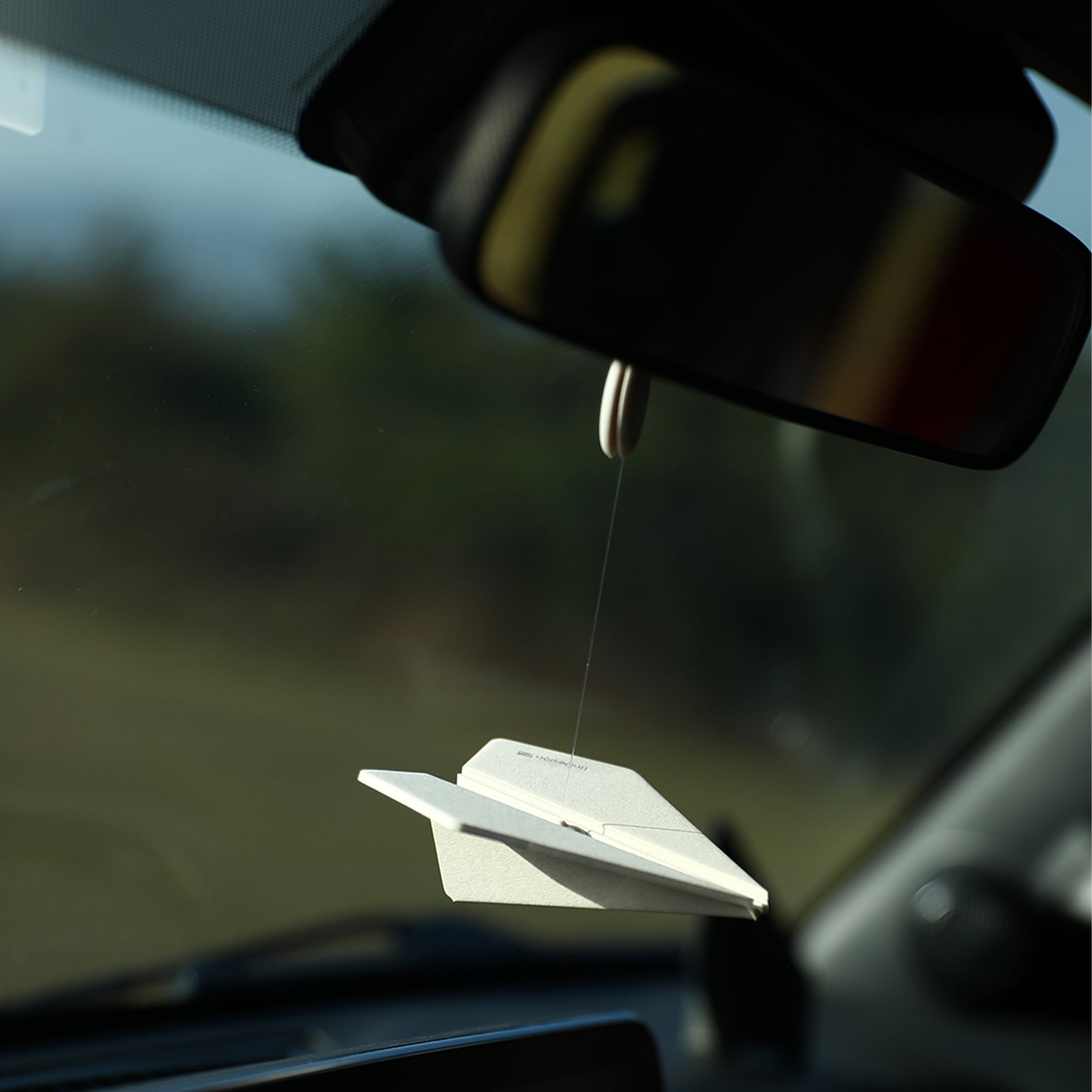 Car air freshener hanging from a car's rearview mirror with a blurred outdoor background